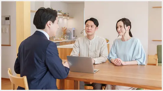 若い夫婦がダイニングテーブルでスーツの男性とノートパソコンを使いながら相談しているシーン